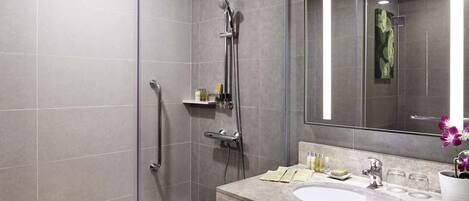 A modern bathroom with a walk-in shower, a large mirror, and a marble sink.