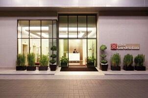 A hotel entrance with a reception desk, glass doors, and potted plants.