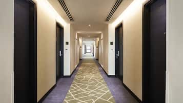 A hotel hallway with carpeted floors, doors on both sides, and a lighted ceiling.