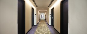 Un pasillo de hotel con pisos alfombrados, puertas a ambos lados y un techo iluminado.