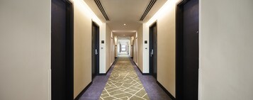 A hotel hallway with carpeted floors, doors on both sides, and a lighted ceiling.