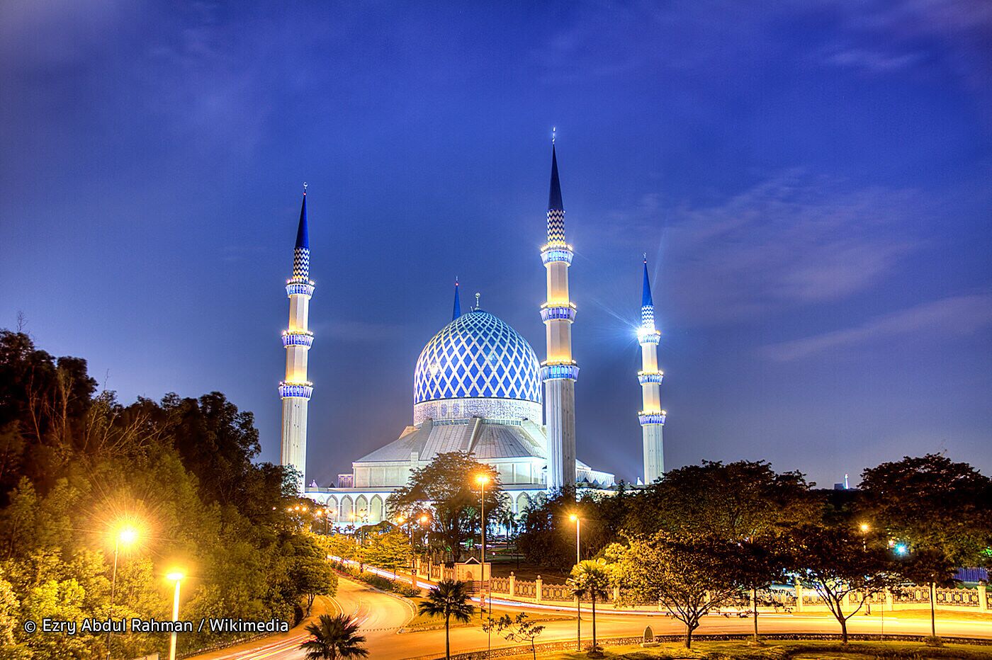 A mosque with a large central dome and four minarets, surrounded by trees and streetlights.