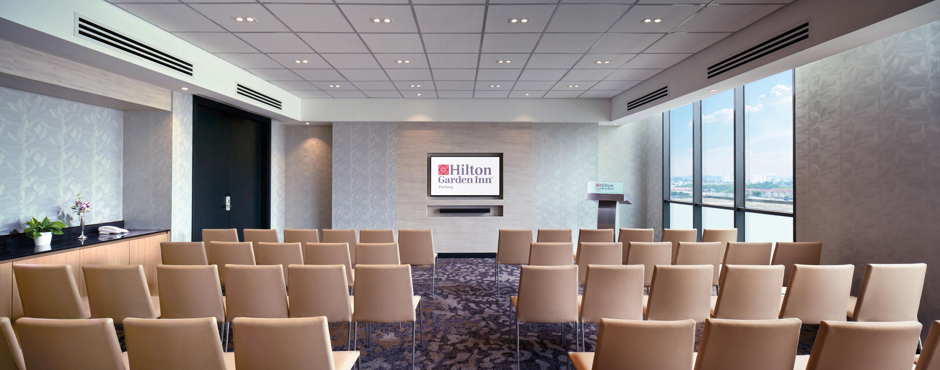 Un salón de conferencias con filas de sillas, un atril y una pantalla que muestra el logotipo de Hilton Garden Inn.