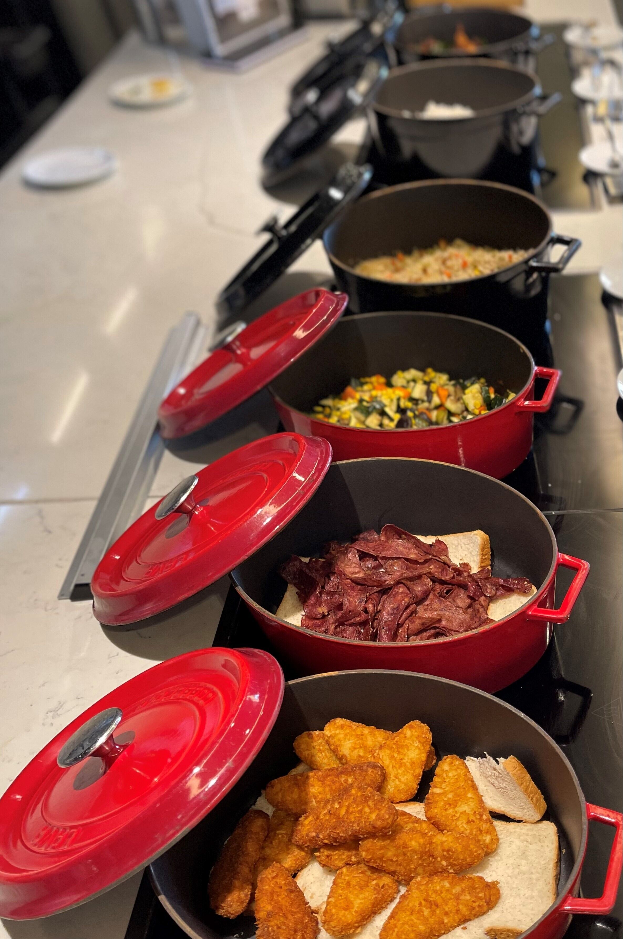 A kitchen counter with various cooking pots and trays of food.