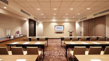 A conference room with multiple tables and chairs, a podium, and a screen displaying the Hilton Garden Inn logo.