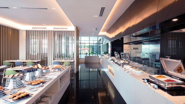 A modern restaurant with a long counter, various food items, and a grill station. - Hilton Garden Inn Puchong (Puchong)