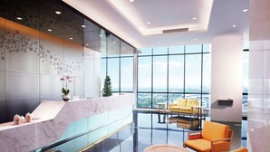 A modern lobby with a marble reception desk, glass partitions, and a seating area with orange chairs. - Hilton Garden Inn Puchong (Puchong)