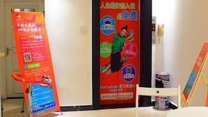Zona de recepción de un hotel con una puerta roja, un mostrador blanco y un cartel promocional en la pared.