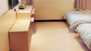 Habitación de hotel con cama, escritorio, silla, televisión y ventana con cortinas.
