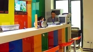 Un mostrador de recepción de colores vivos con una pantalla de televisión, una computadora y una persona sentada detrás.
