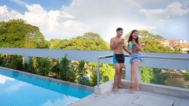 Une piscine dotée d’une balustrade en verre, entourée d’une végétation luxuriante et surplombée par un ciel dégagé.