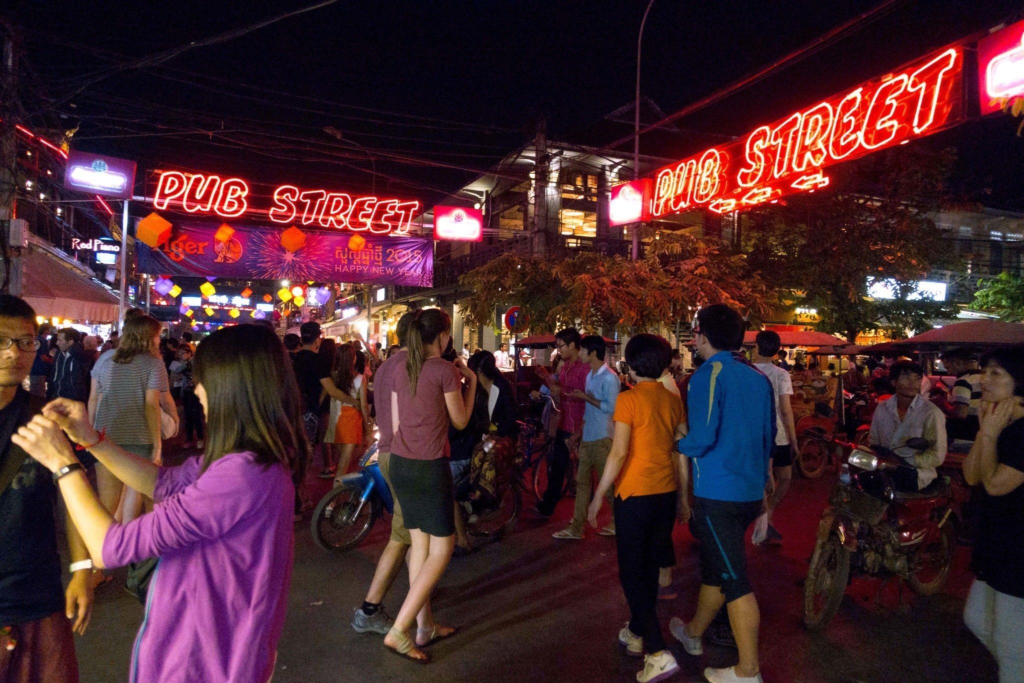 Una calle concurrida con letreros de neón que indican 'PUB STREET' y 'PUB STREET', señal de una zona de vida nocturna.