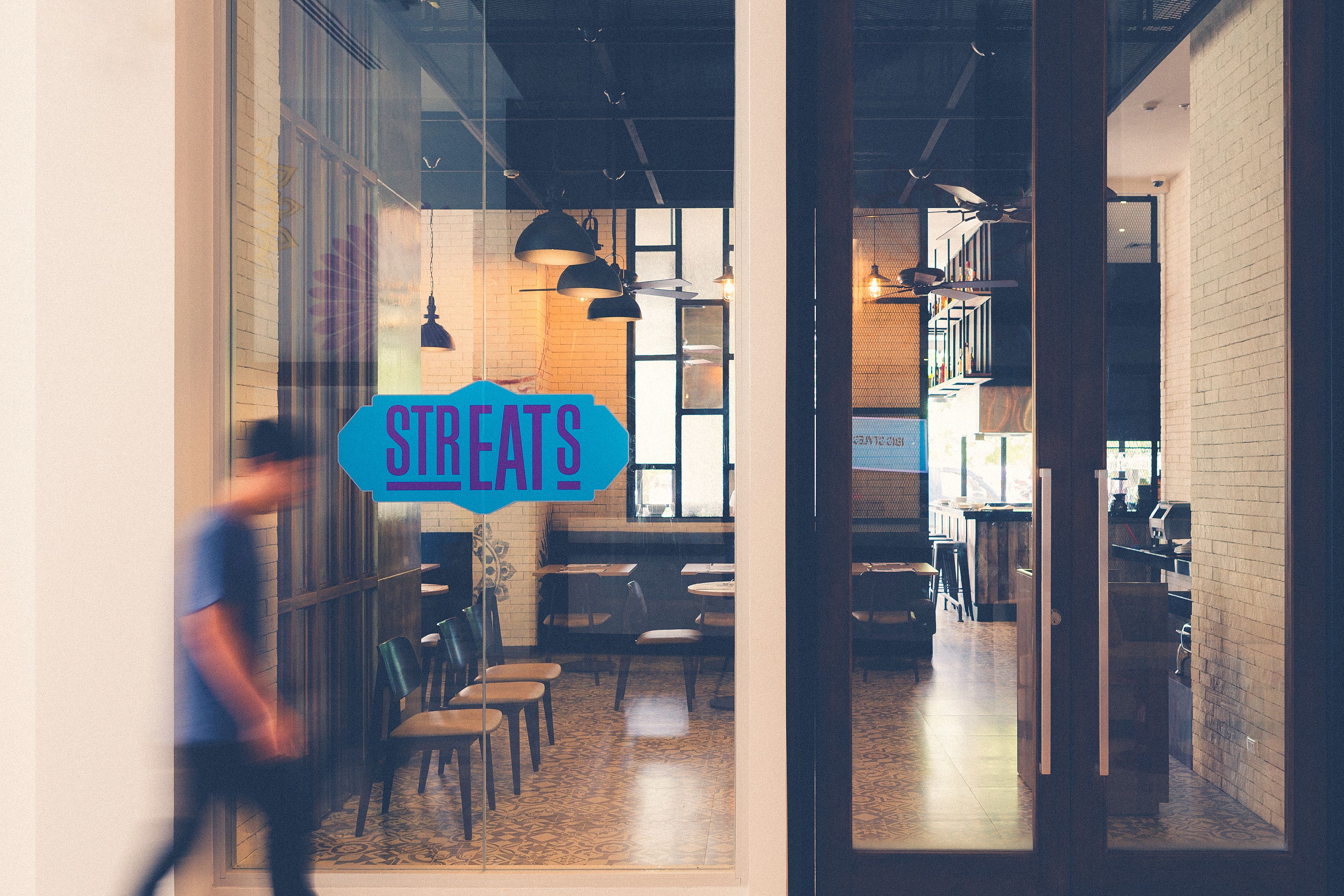An interior view of a restaurant with a glass partition, tables, chairs, and hanging lights.