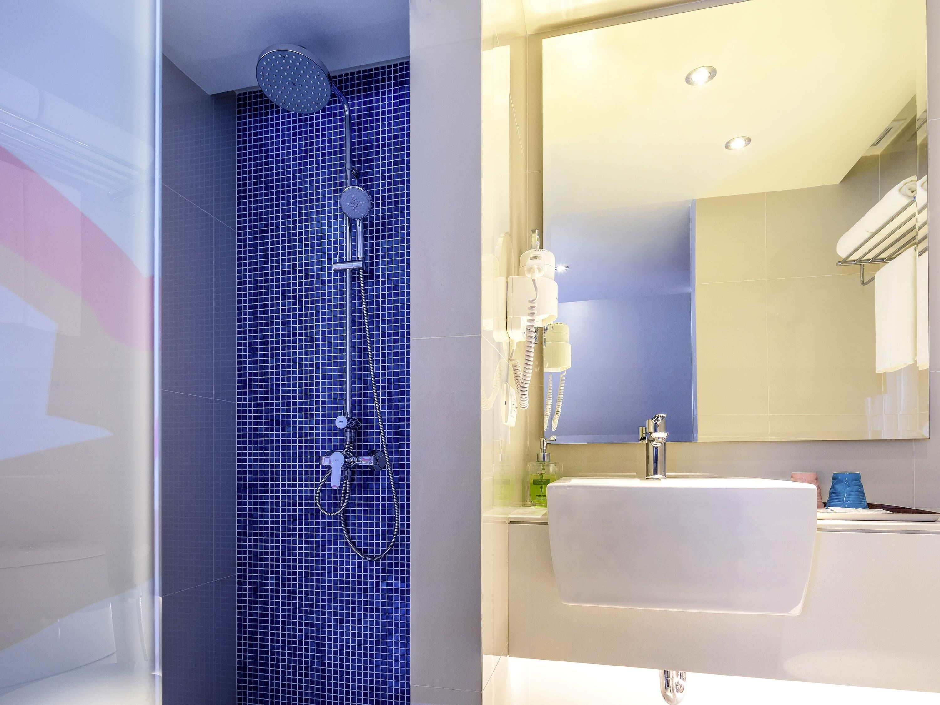 A bathroom with a blue-tiled shower, a white sink, and a mirror above the sink.