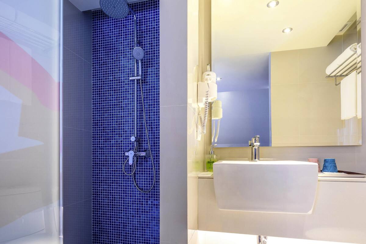 A bathroom with a blue-tiled shower, a white sink, and a mirror above the sink.