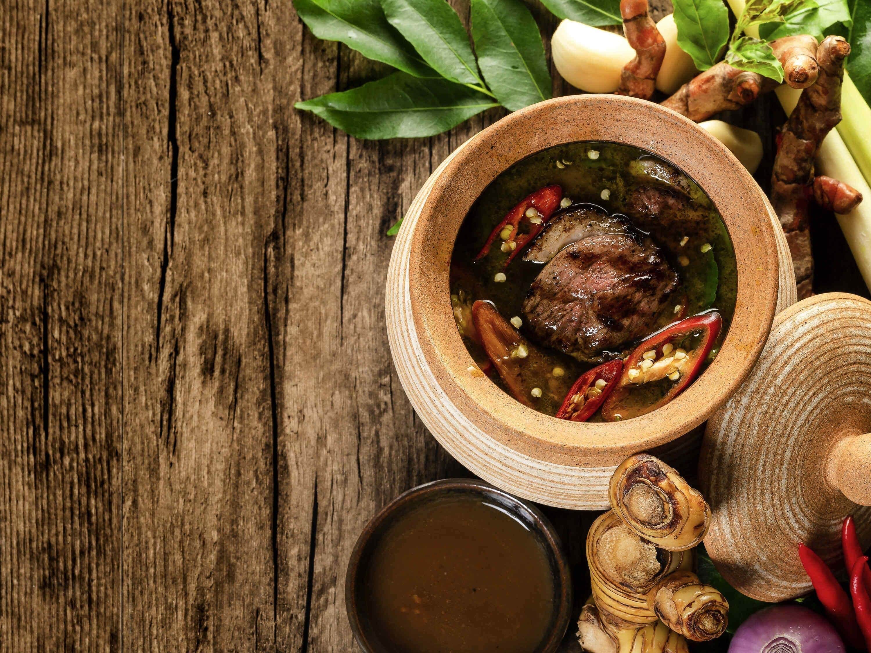 A bowl of meat with spices and a small bowl of sauce on a wooden surface.