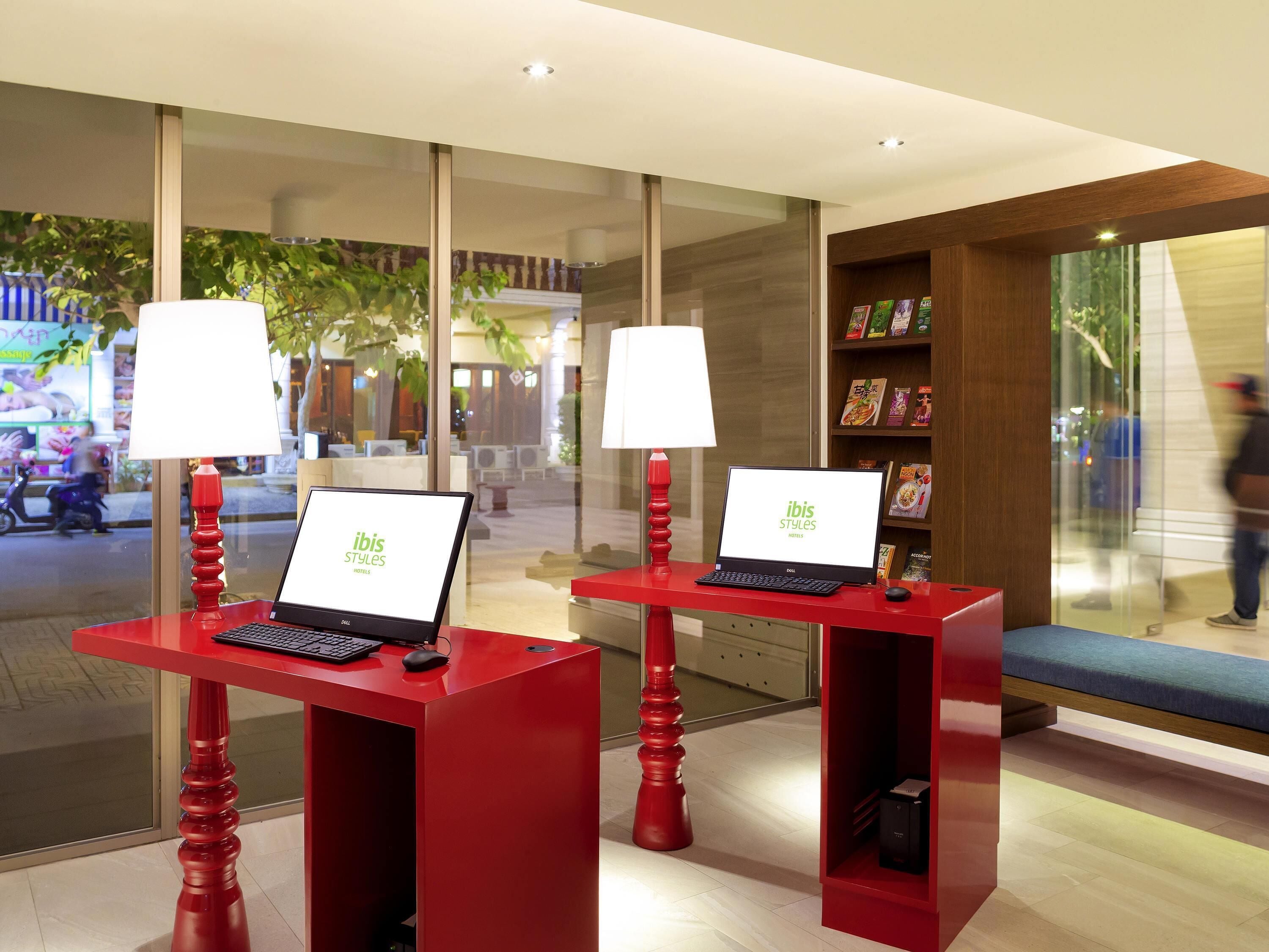 A hotel reception area with two red desks, each with a laptop and a lamp.