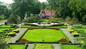 Un jardin à la française avec une pelouse centrale, des allées et un bâtiment doté d’un toit rouge en arrière-plan.