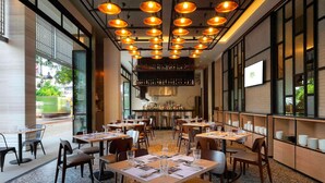 L’intérieur d’un restaurant avec de nombreuses tables, des chaises, des luminaires suspendus, un bar et de grandes fenêtres.
