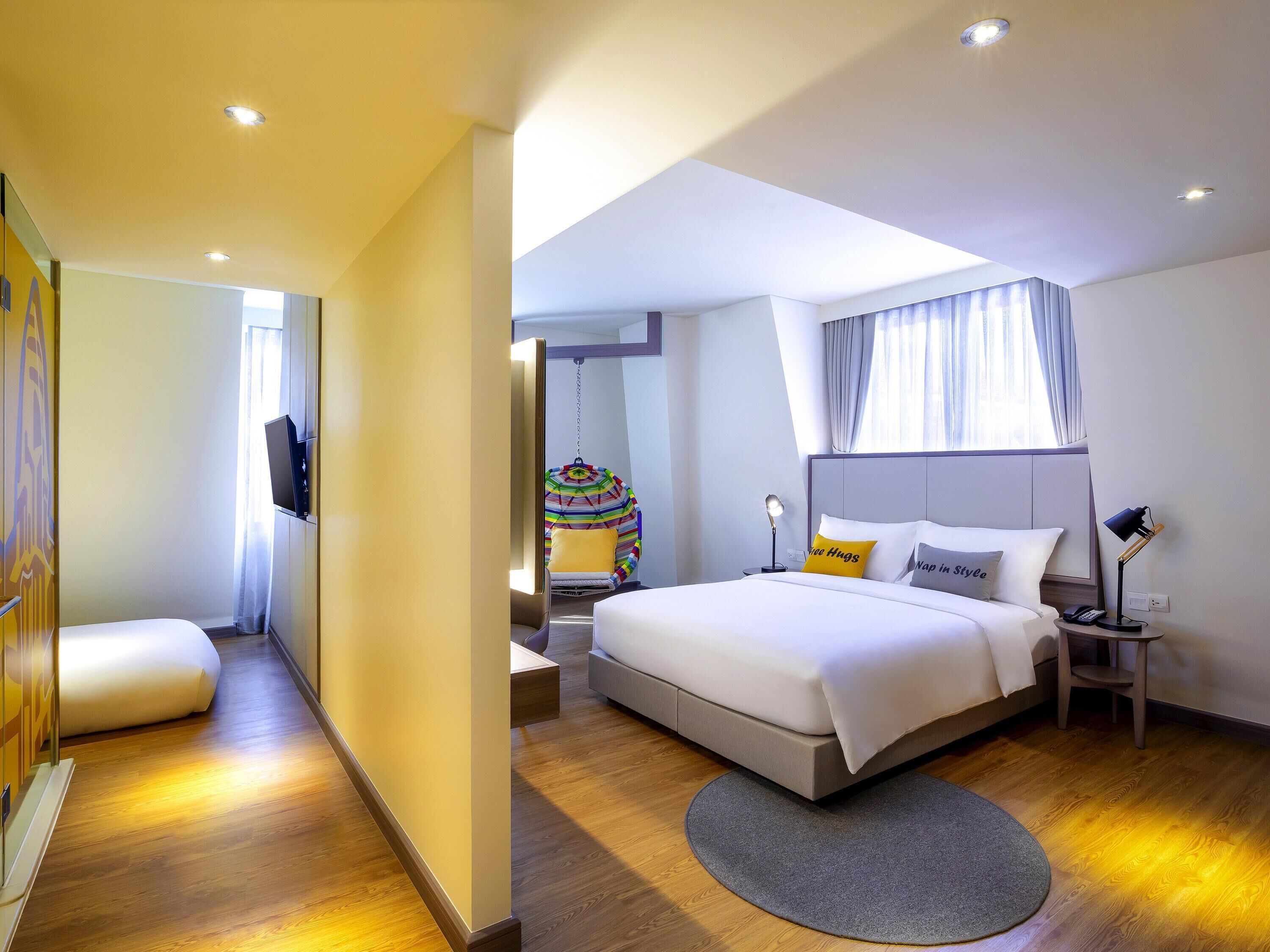 Quarto de hotel com cama, mesas de cabeceira, cadeira suspensa e televisão.