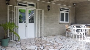 A covered patio with a tiled floor, a white table and chairs, a potted plant, and a gate with a view of a staircase and greenery. - Campeche Villa (Mero)