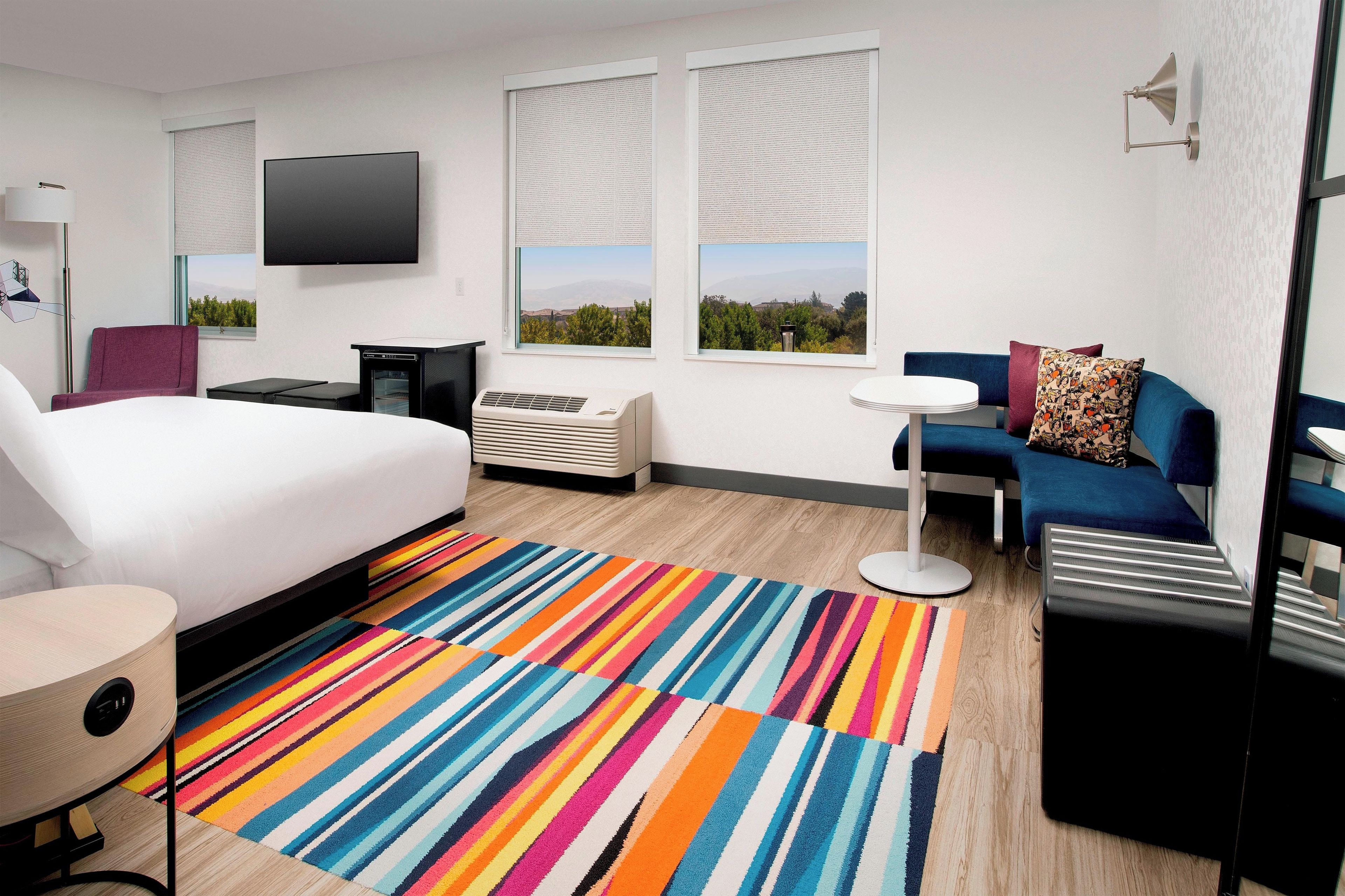 Habitación de hotel con cama, escritorio, sofá, televisión y ventana con vistas.