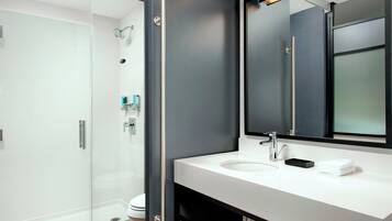Un baño moderno con cabina de ducha de vidrio, lavamanos blanco y un espejo grande.