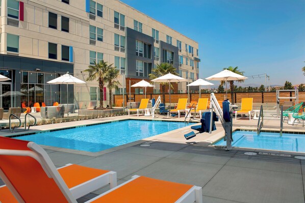 A swimming pool with lounge chairs and umbrellas, surrounded by a building with multiple windows. - Aloft by Marriott Dublin-Pleasanton (Dublin)