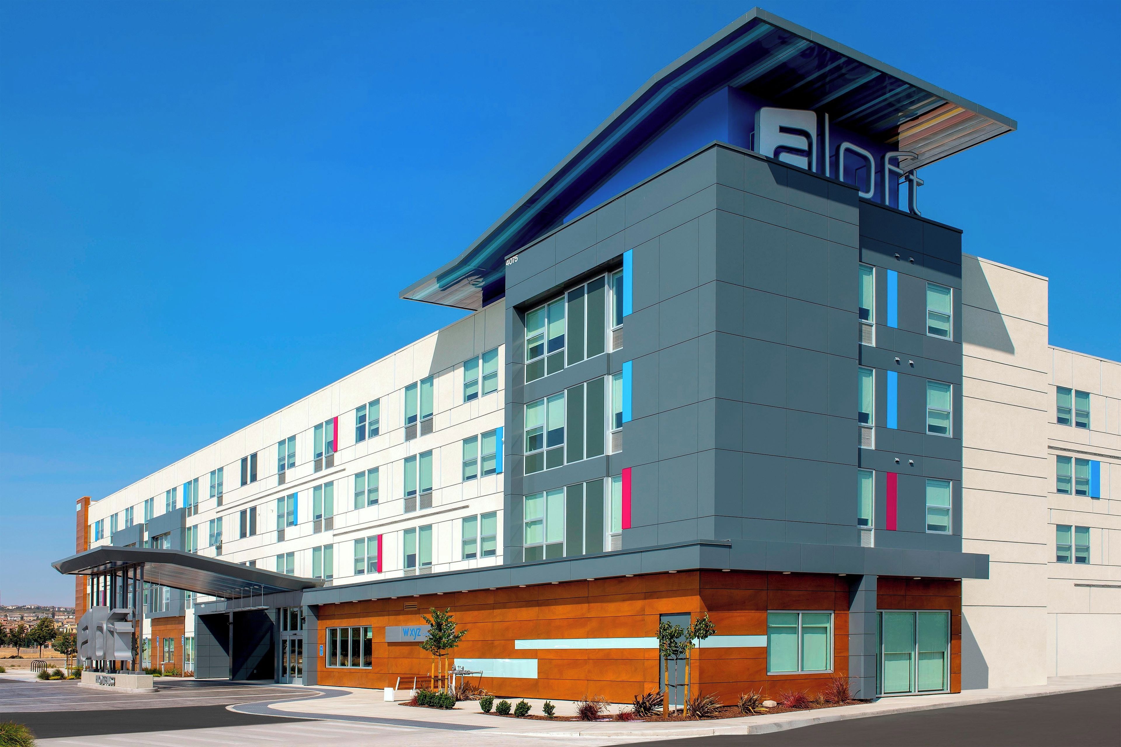 A modern multi-story building with a flat roof, large windows, and a prominent entrance with a covered walkway.