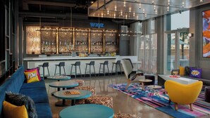 Un área de bar moderna con un letrero de neón, taburetes y una zona de estar con sofás y mesas redondas.