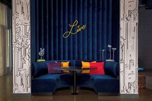 A room with a dark blue velvet sofa, a small round table, and a neon sign that reads 'Live'. - Aloft by Marriott Dublin-Pleasanton (Dublin)