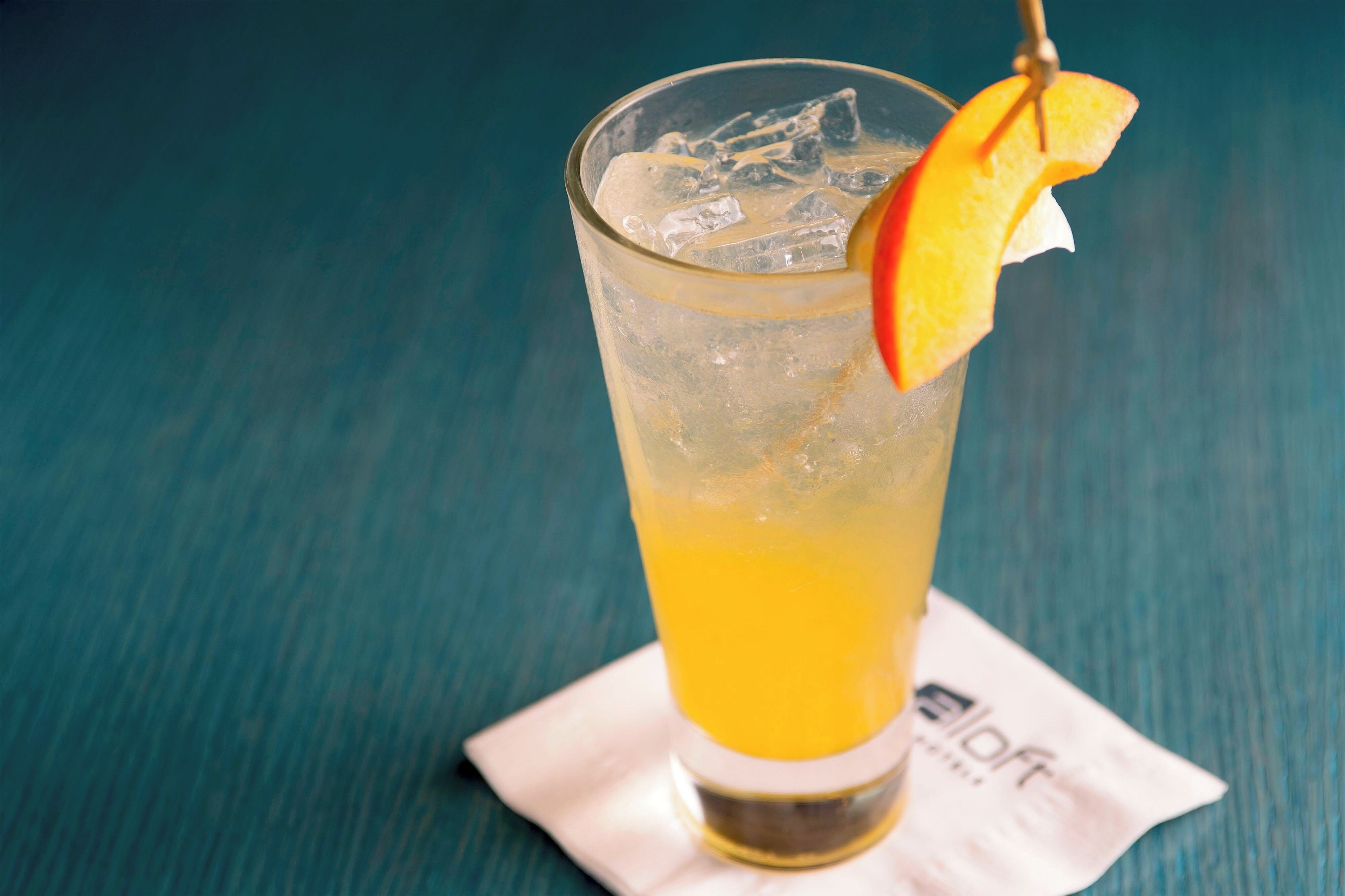 Um copo de suco de laranja com gelo e uma fatia de laranja sobre um guardanapo.