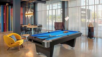 A pool table in a well-lit room with large windows, a yellow armchair, and a billiards rack.