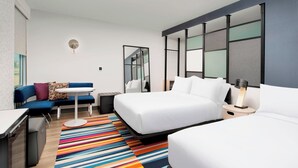 Una habitación de hotel moderna con una cama grande, un sofá, un escritorio y un tapete colorido a rayas.