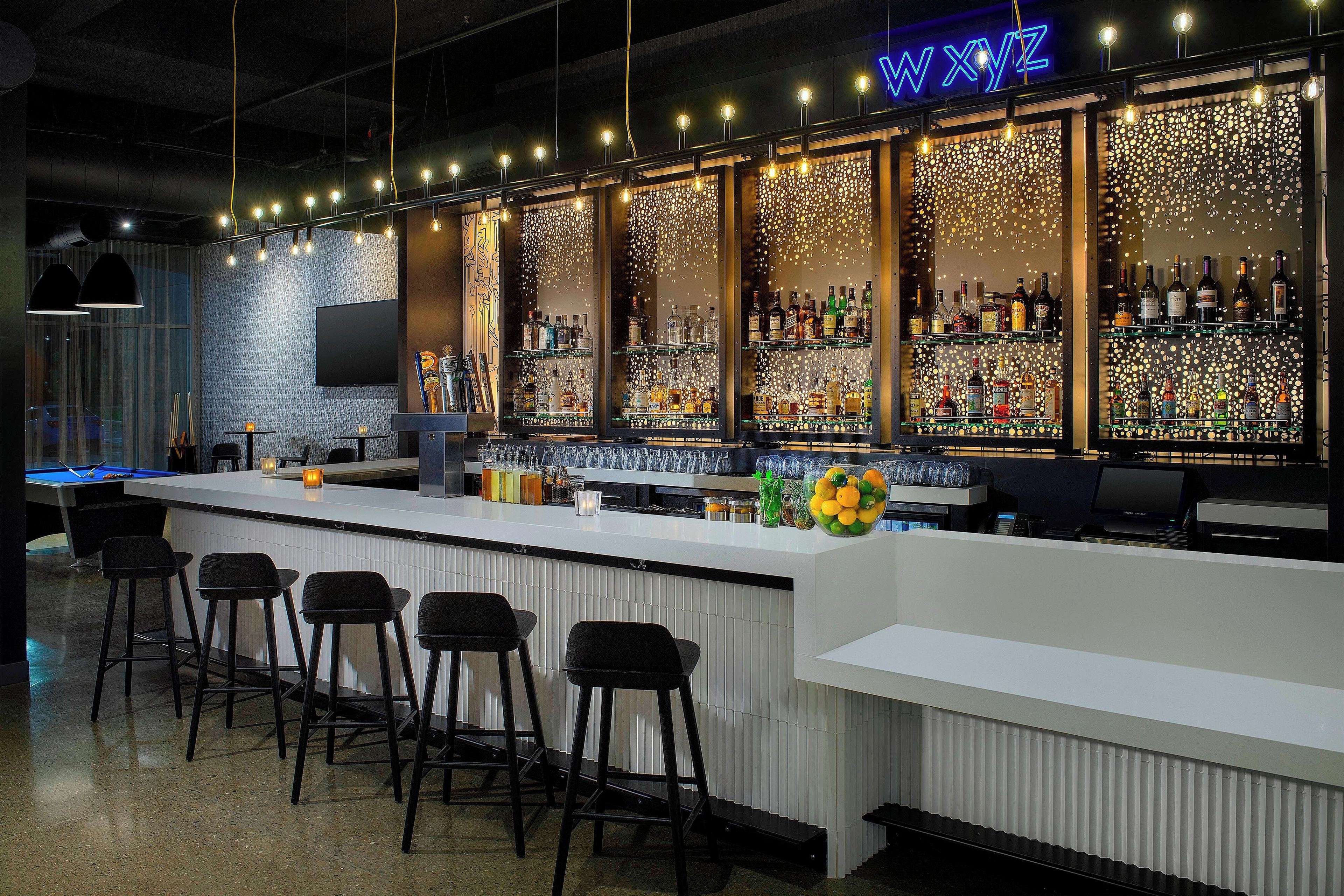 A bar area with a pool table, bar stools, and a variety of liquor bottles.