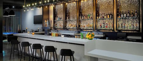 A bar area with a pool table, bar stools, and a variety of liquor bottles.