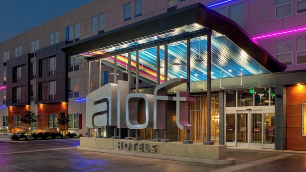Entrada moderna de un hotel con un gran letrero 'aloft', puertas de vidrio y un área de acceso cubierta.