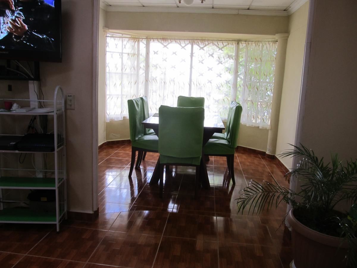 Uma área de refeições com mesa e cadeiras, uma TV na parede e um vaso com planta.