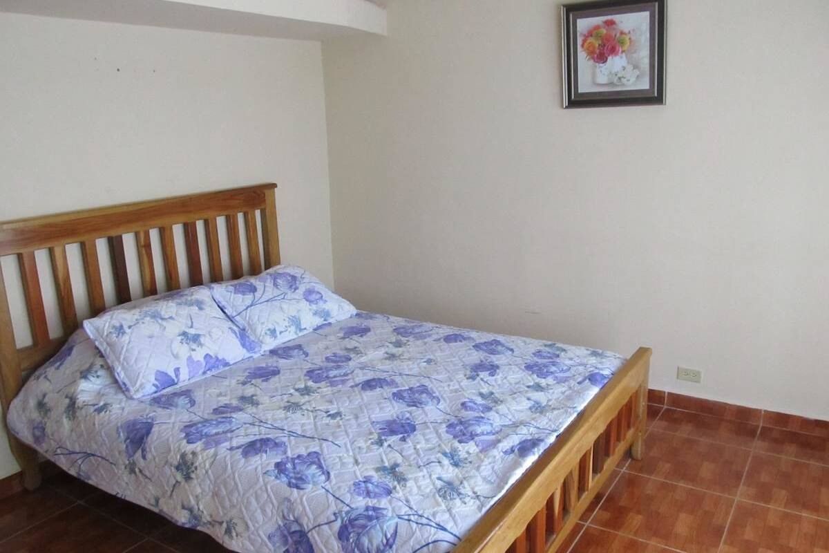 A single bed with a floral bedspread in a room with a tiled floor and a white wall.