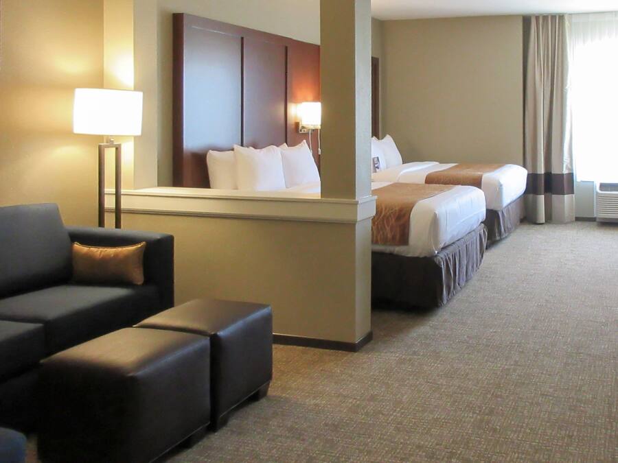 Una habitación de hotel con sofá, cama con cabecera, mesita de noche y lámpara.