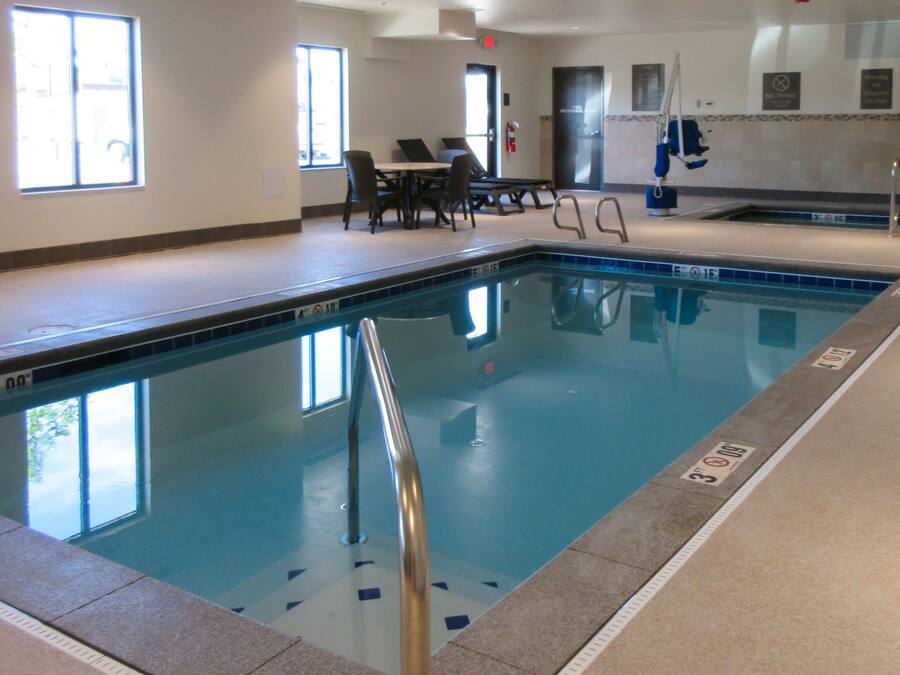 Una piscina interior con carriles delimitados, una silla de socorrista y una zona de estar con mesas y sillas.