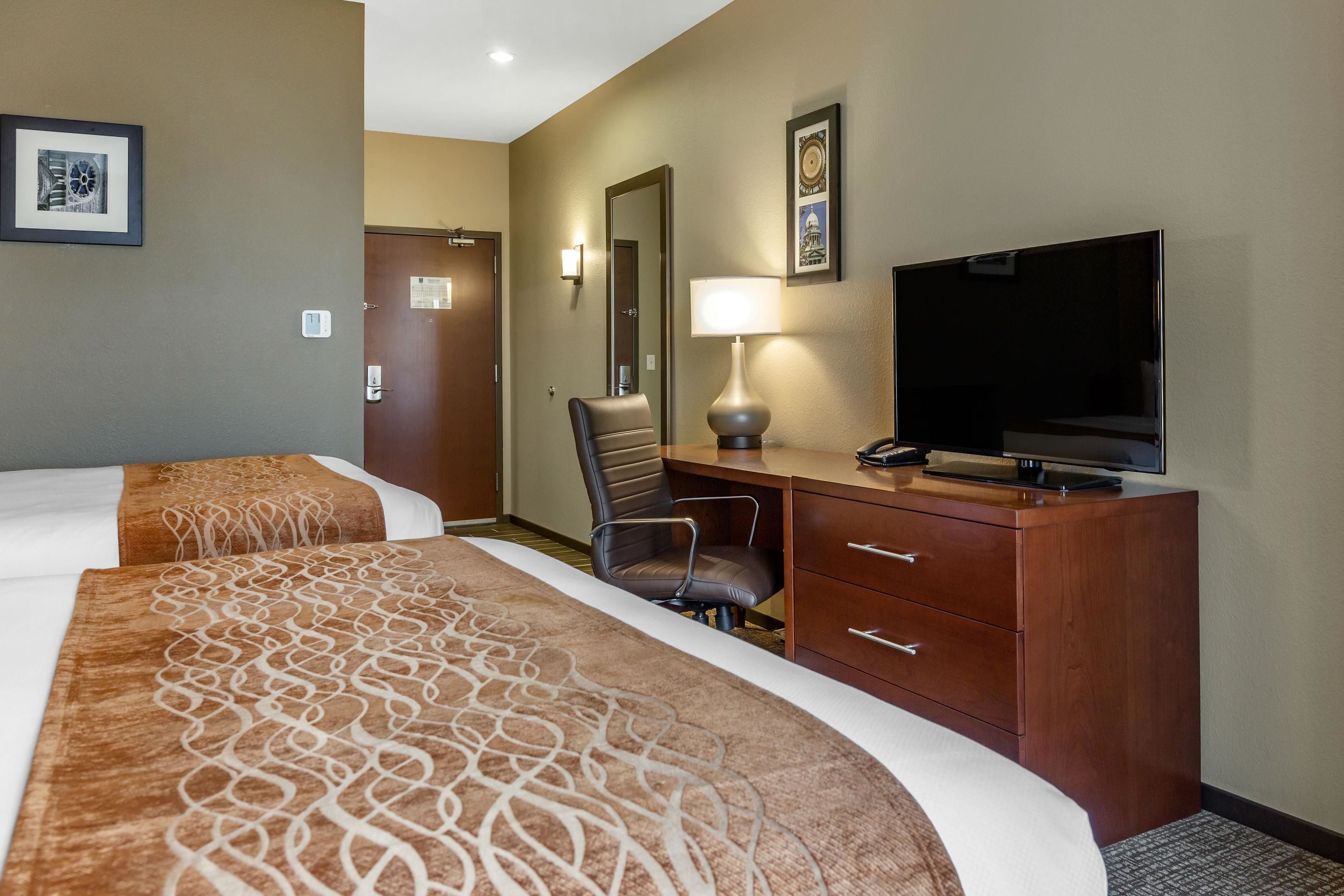 Une chambre d’hôtel avec deux lits, un bureau équipé d’une télévision, une chaise et une lampe.