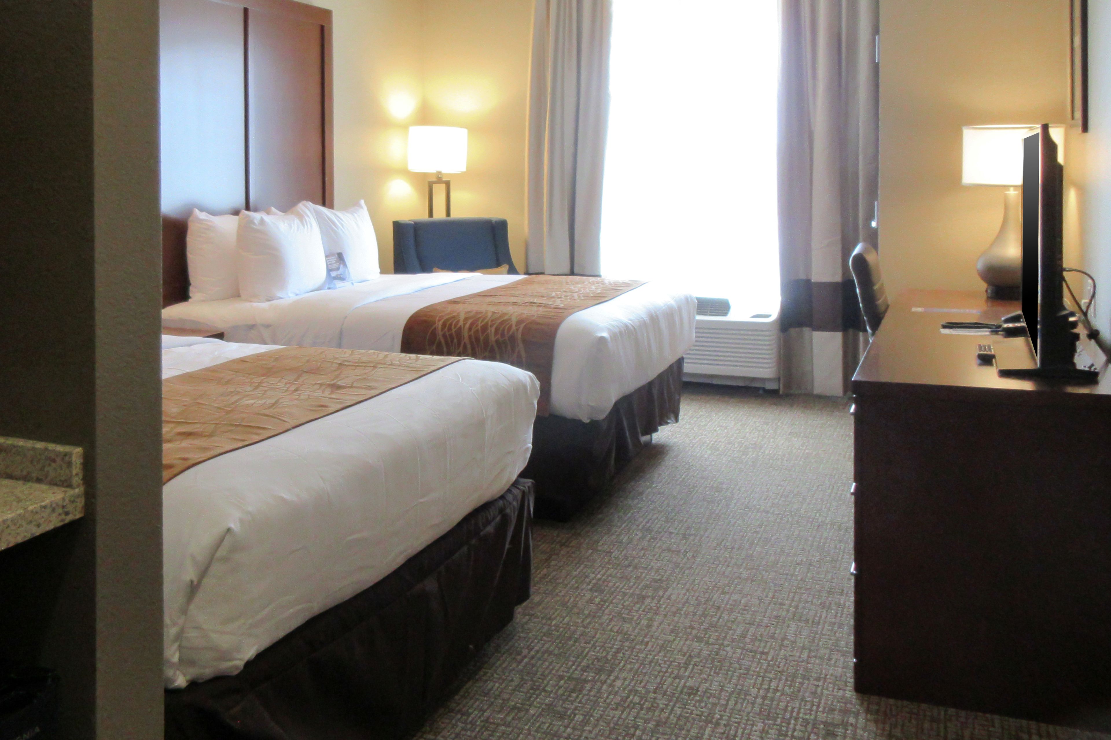 Une chambre d’hôtel avec deux lits, un bureau avec un ordinateur et une fenêtre avec des rideaux.