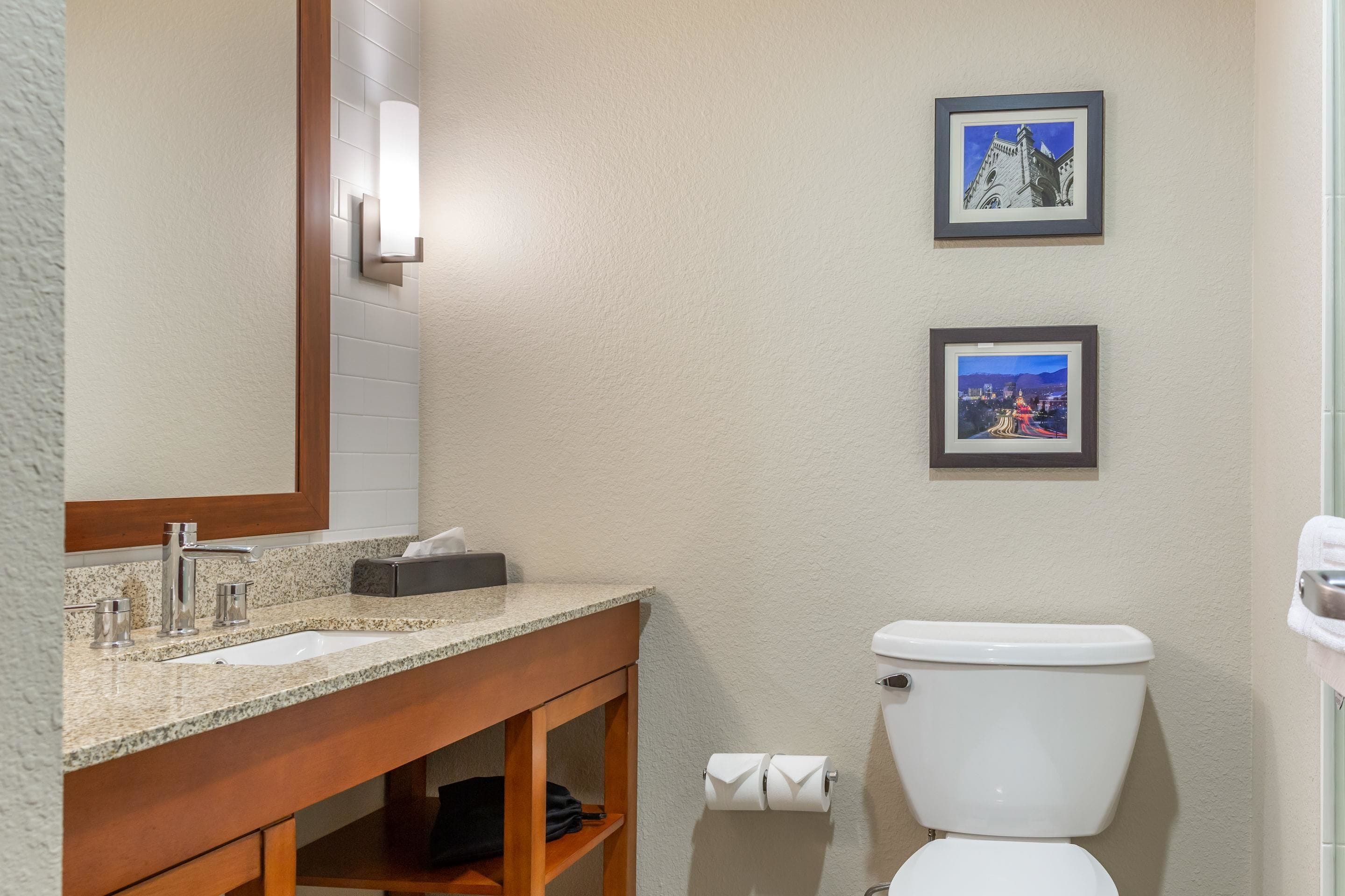 A bathroom with a sink, mirror, toilet, and two framed pictures on the wall.