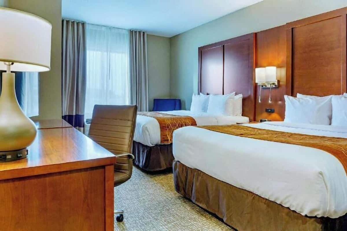 Una habitación de hotel con dos camas, un escritorio, una silla, una lámpara y una ventana con cortinas.