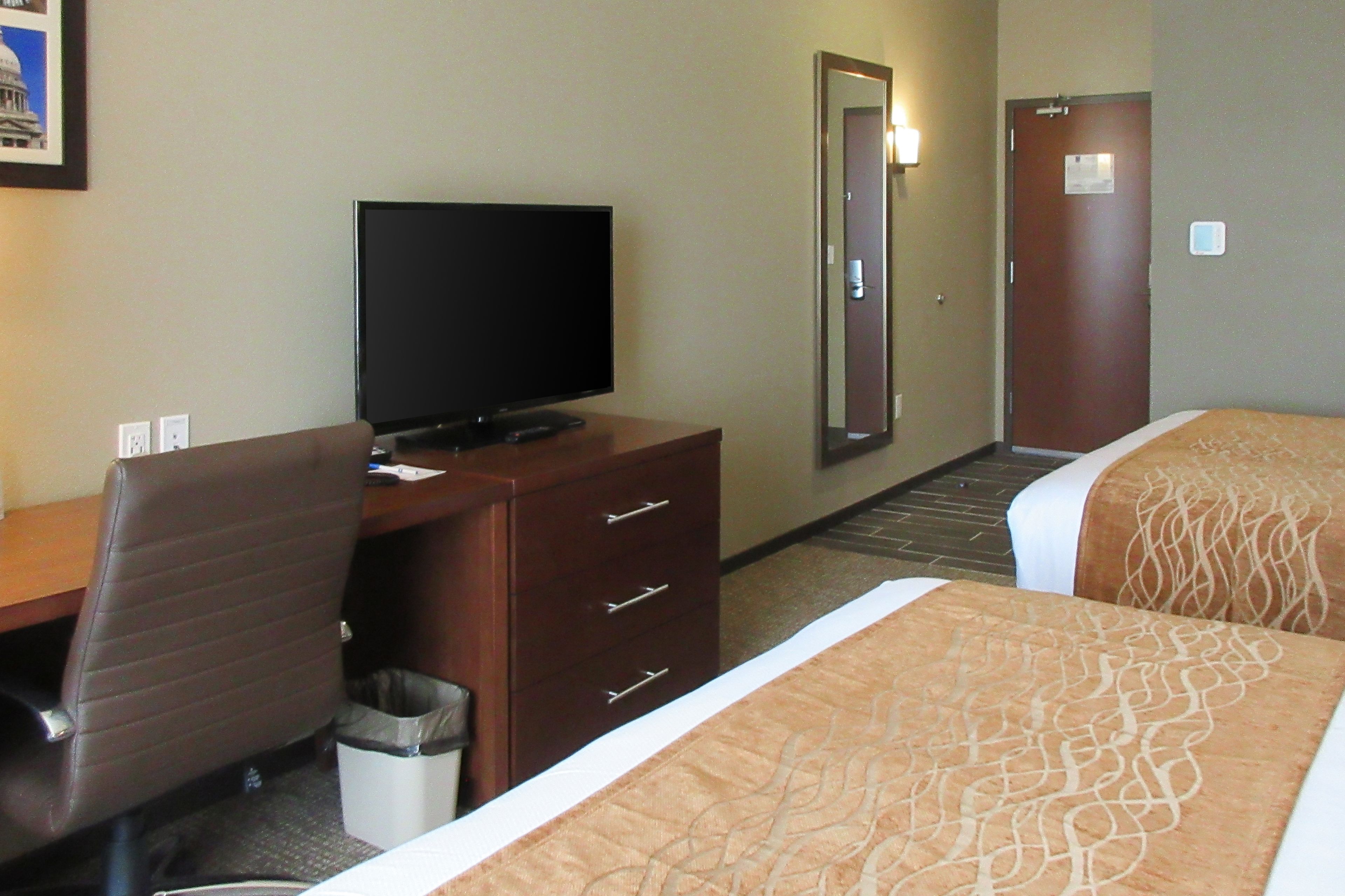 Una habitación de hotel con una cama, un escritorio con televisor, una silla y un cubo de basura.