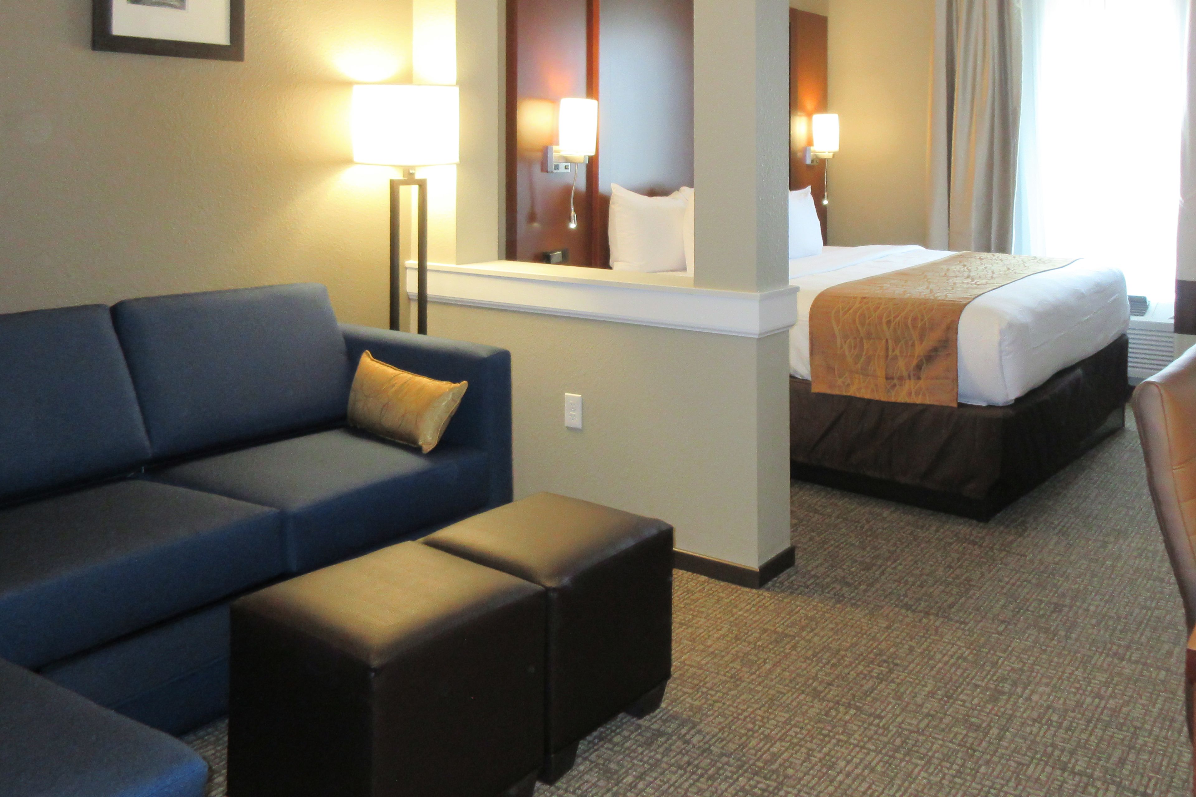 A hotel room with a bed, a blue sofa, a small table, and a mirror.