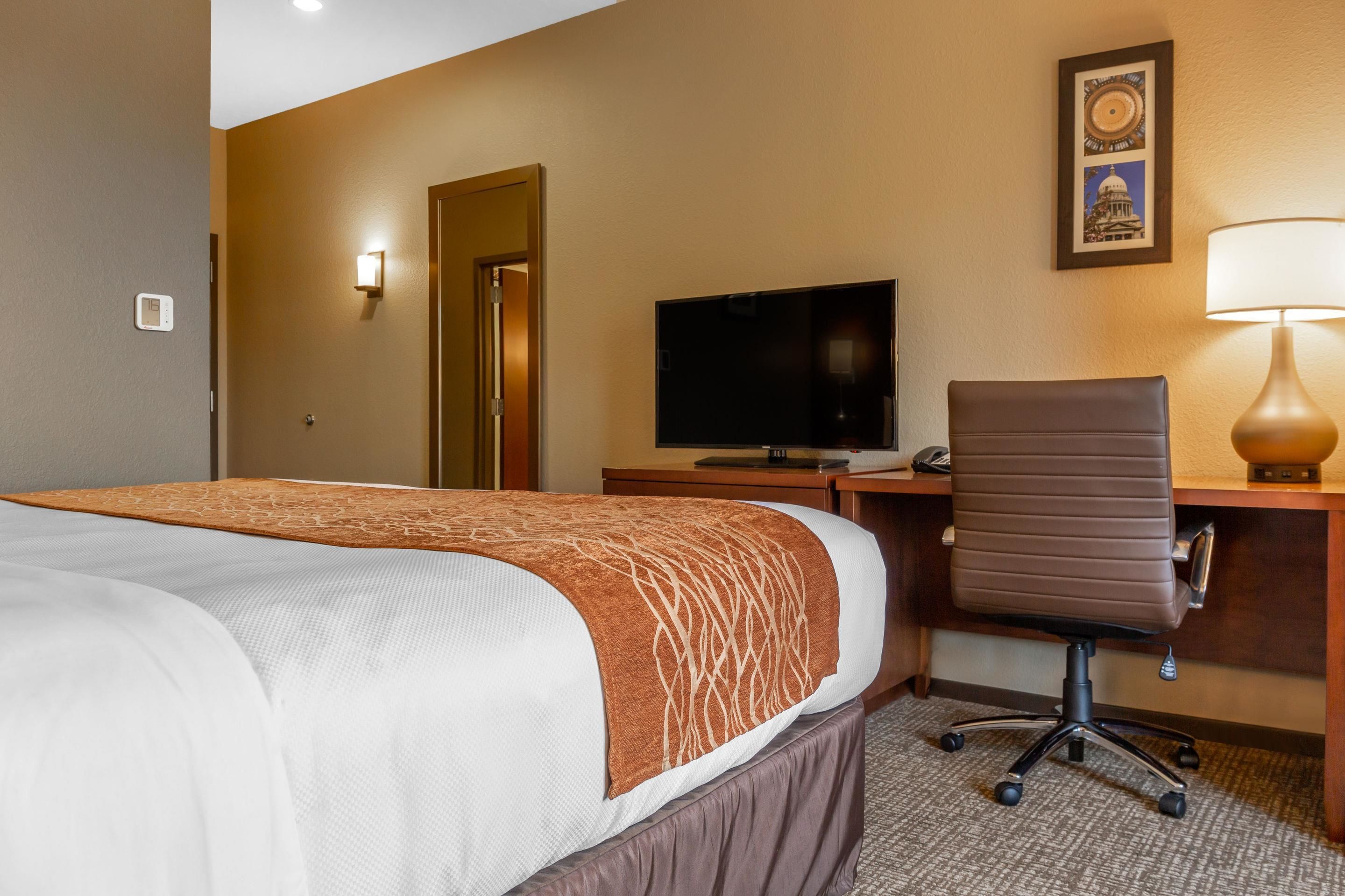 A hotel room with a bed, a desk with a computer, a chair, a television, and a lamp.