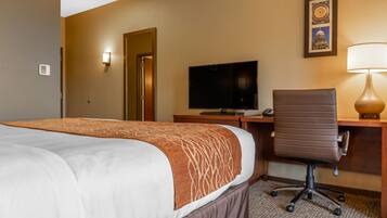 A hotel room with a bed, a desk with a computer, a chair, a television, and a lamp.