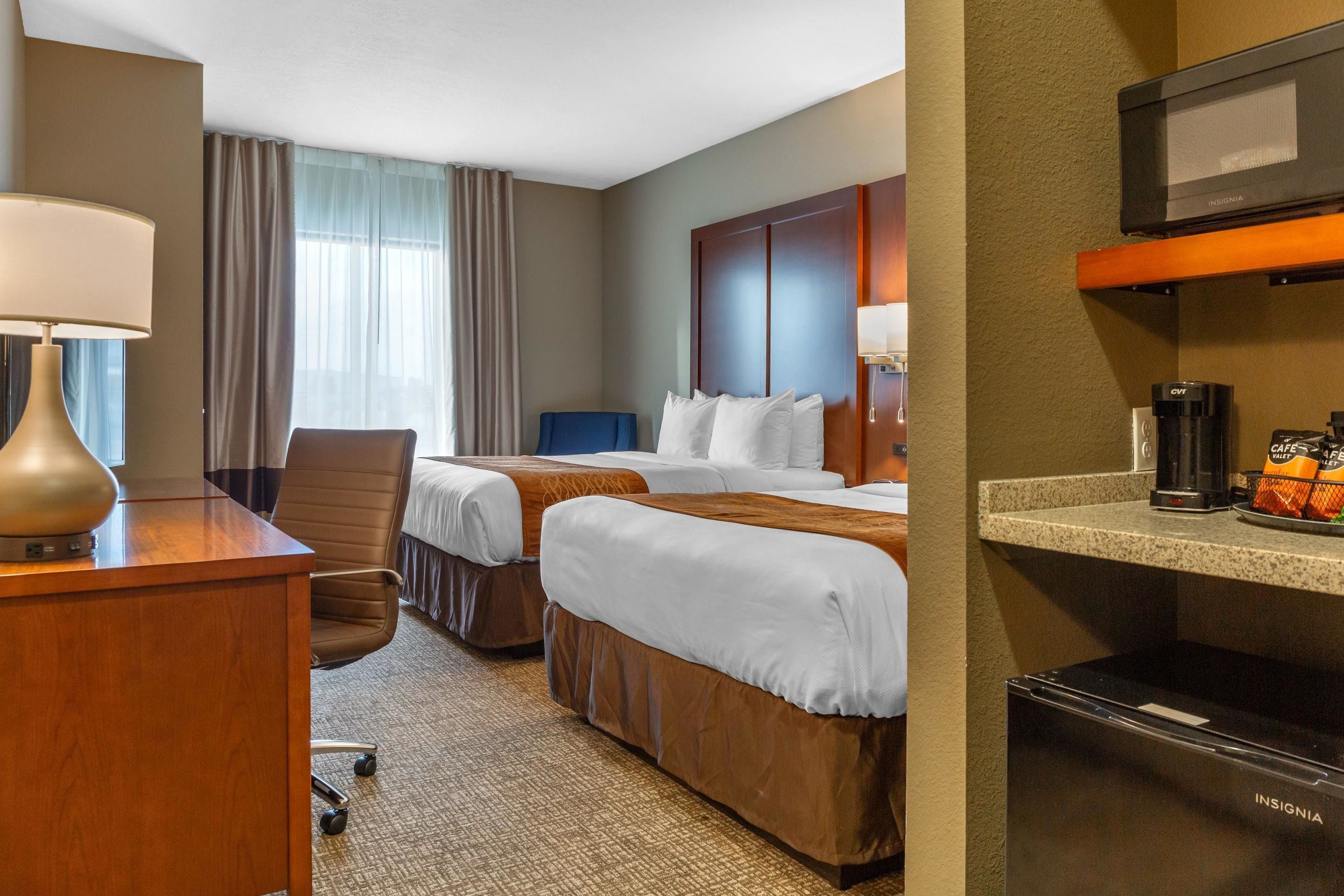 A hotel room with two beds, a desk, a chair, a coffee maker, and a TV.
